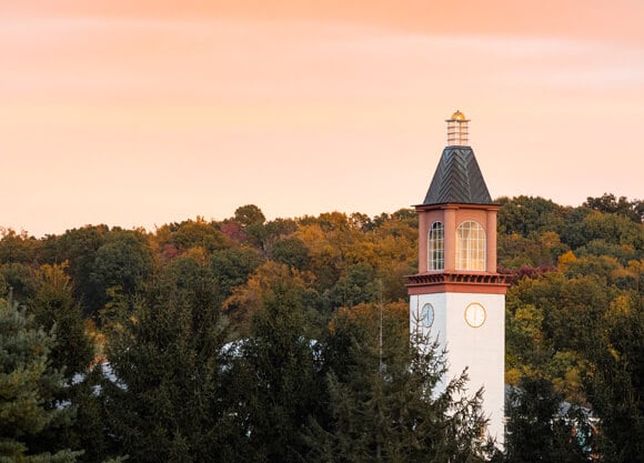 Quinnipiac library clocktower in front of a pink and orange sunset sky