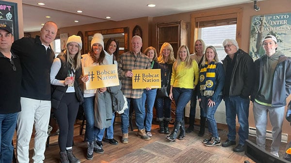 group of people holding signs and smiling at a Quinnipiac athletics event