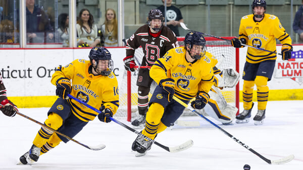 Quinnipiac men's ice hockey players skate across the ice with the puck during a game