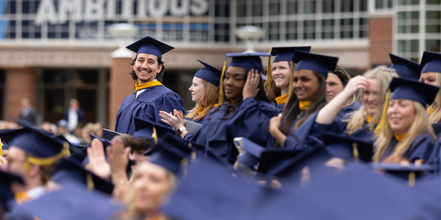 Dozens of grads stand, smile and cheer during a Quinnipiac Commencement ceremony