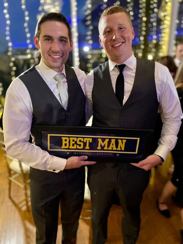 Mark Spillane and Charlie Doe in formal wear hold best man sign at a wedding