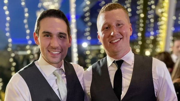 Mark Spillane and Charlie Doe in formal wear hold best man sign at a wedding