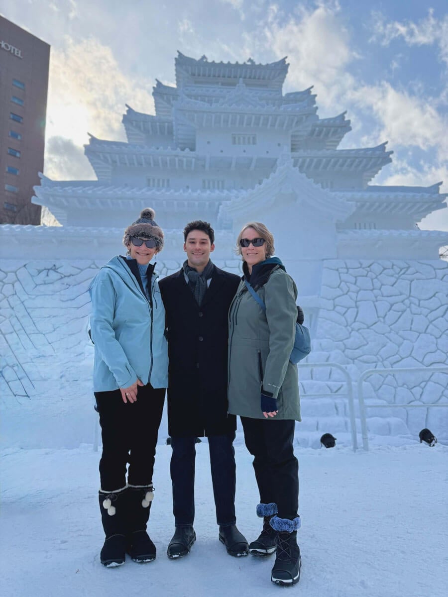 Three Quinnipiac alums in winter coats pose for a photo in front of an ice sculpture