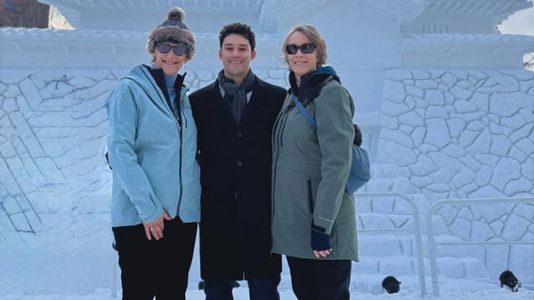 Three Quinnipiac alums in winter coats pose for a photo in front of an ice sculpture