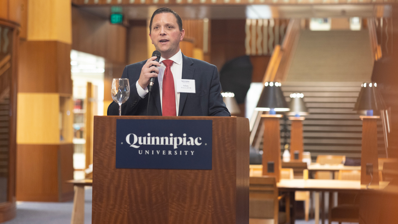 Adam Swanson, JD '08, speaks with a microphone at a podium in the School of Law atrium