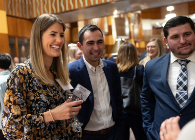 Three law alumni with name tags smile and talk in the Quinnipiac Law library atrium during a reception event