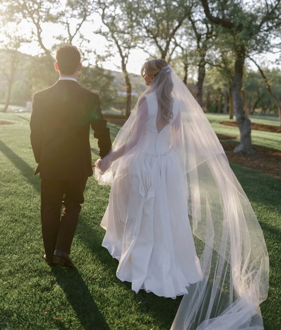 Two people holding hands and looking into the distance, one wearing a suit and the other a wedding dress