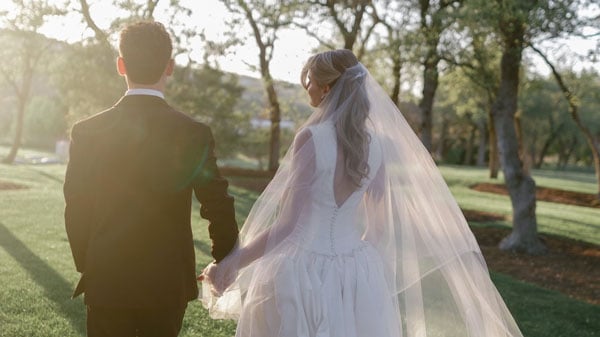 Two people holding hands and looking into the distance, one wearing a suit and the other a wedding dress