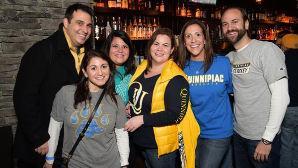 A group of alumni in Quinnipiac gear pose for a photo at a reception in a local pub