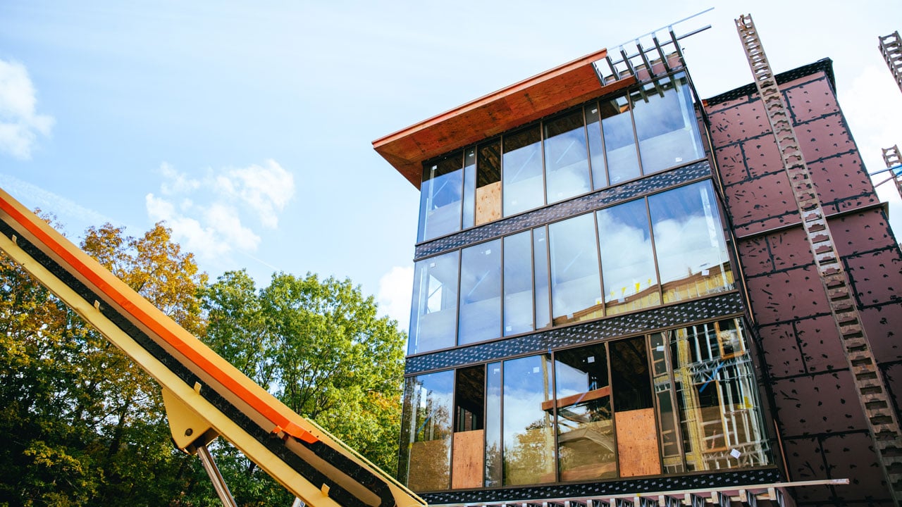 Trees and equipment surround one of the new south quad buildings with many windows.