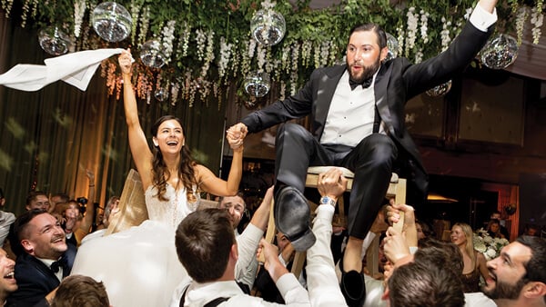 Alex Leafer and wife are lifted on chairs by a crowd of people on their wedding day