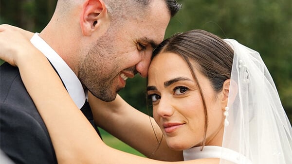 Savannah Reilly looks at the camera as her husband embraces her on their wedding day