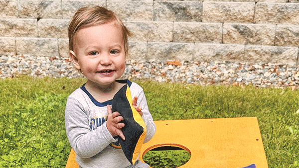 Baby Rigazio in a Bobcats outfit smiles and sits on a Quinnipiac bean bag toss game board