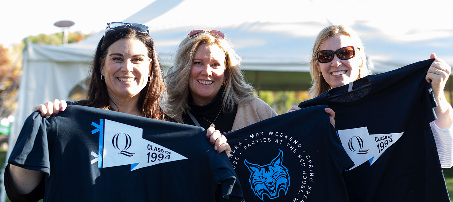 Three alumni hold up tee shirts with a Quinnipiac Class of 1994 pennants design