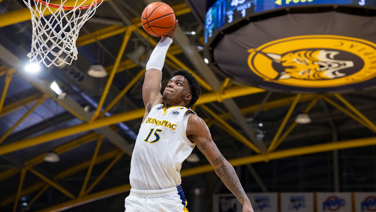 A Quinnipiac basketball player makes a shot with the scoreboard in the background