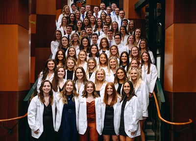 Physical therapy class pose for photo in white coats on lobby stairs of North Haven Campus