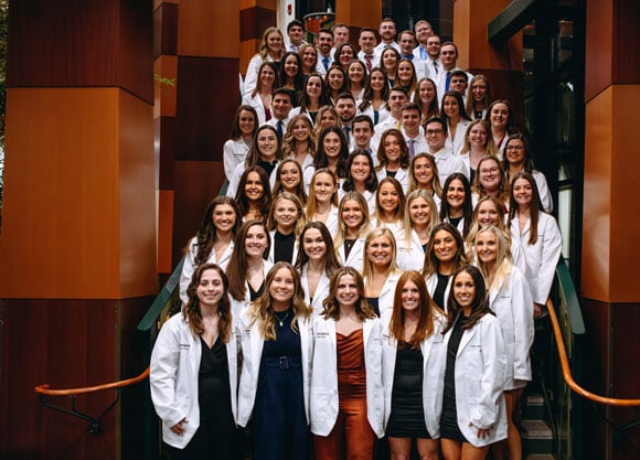 Physical therapy class pose for photo in white coats on lobby stairs of North Haven Campus