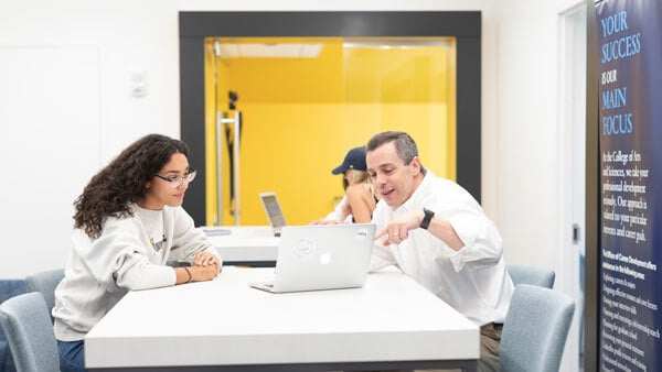 A professor and student talking with a laptop in front of them in the career advisement center