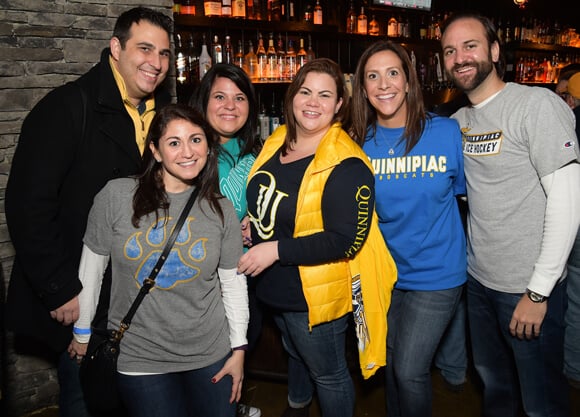 A group of alumni in Quinnipiac gear pose for a photo at a reception in a local pub